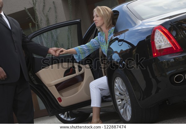 Chauffeur helps\
woman to get down from luxury\
car