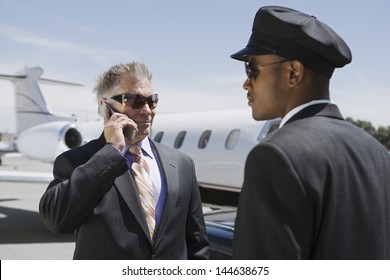 Chauffeur Looking At Senior Businessman On Call With Private Jet In The Background