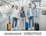 Cheap Flights Offer. Three Joyful Guys With Travel Suitcases Holding Their Passports With Tickets And Boarding Passes Standing In Modern Airport Indoors, Smiling To Camera. Full Length