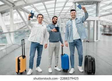 Cheap Flights Offer. Three Joyful Guys With Travel Suitcases Holding Their Passports With Tickets And Boarding Passes Standing In Modern Airport Indoors, Smiling To Camera. Full Length - Shutterstock ID 2288379425