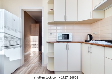 Cheap Simple Interior Of Empty Kitchen With Wooden Furniture, White Fridge, Gas Stove, And Microwave. Rostov-on-Don, Russia - 10 November 2020.