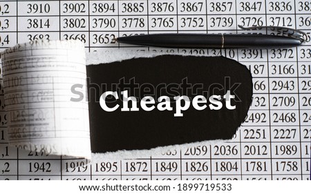 CHEAPEST is the word behind torn office paper with numbers and a black pen. Business and finance concept