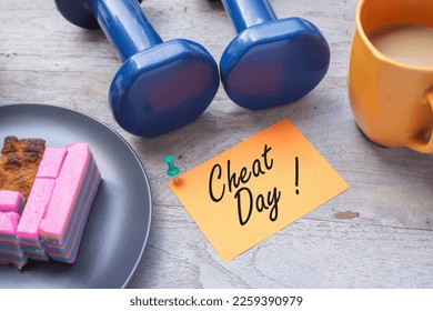 Cheat Day! concept with message written on a piece of paper. Dump-bells, a cup of coffee, and sweet Malay cakes at the side.