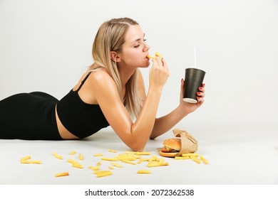 Cheat Meal Concept. Athlete Woman Is Posing With Fast Food On Light Gray Background, Studio Shot. Young Sporty Woman Is Eating Fast Food