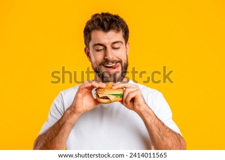 Cheat Meal. Portrait Of Funny Hungry European Man Eating Tasty Cheeseburger, Standing Against Yellow Background In Studio. Junk Food Nutrition, Concept Of Unhealthy Meals