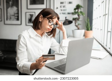 Cheated and disappointed young businesswoman working in cozy office or cafe, holding bank credit card and trying to make purchase, online fraud and deception - Shutterstock ID 2307223005