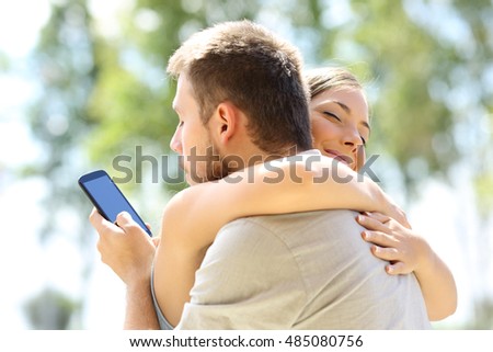 Cheater texting with his other lover on phone and hugging his innocent girlfriend