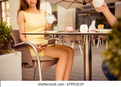 Cheating concept. Young elegant lady is texting to her lover secretly while sitting with the husband in summer terrace cafe, having brunch out