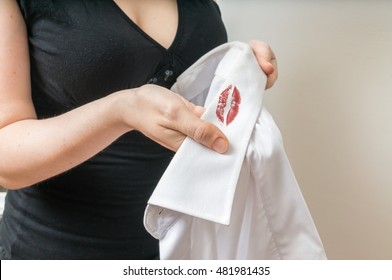 Cheating and infidelity concept. Woman holds white shirt of her husband with red lipstick stains on collar.