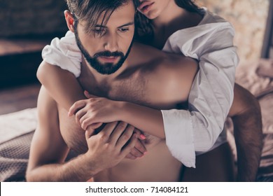 Cheating, jealous, obsession, possession concept. Handsome sad half naked young guy is looking down, thinking about cheating to his wife with gorgeous lover, who hugs him from the back, cropped photo
