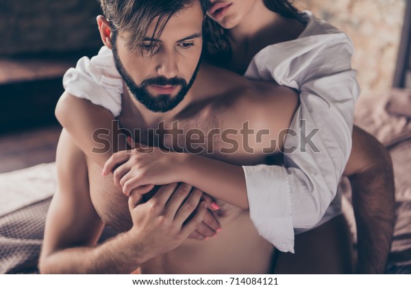 Cheating, jealous, obsession, possession concept.\
Handsome sad half naked young guy is looking down, thinking about\
cheating to his wife with gorgeous lover, who hugs him from the\
back, cropped photo