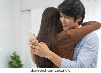 Cheating on girlfriends concept, unfaithful Asian man looking at mobile phone text during embracing with his lover