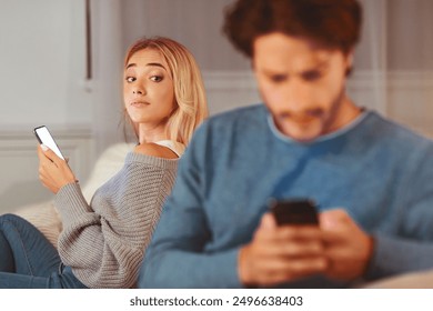 Cheating Signs. Girl Looking At Her Boyfriend Texting On Phone Suspecting Infidelity Sitting On Couch At Home. Selective Focus - Powered by Shutterstock