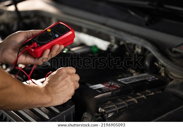 Check\
battery voltage with electric multimeter. Man using multimeter to\
measure the voltage of the batteries. Mechanic doing car\
inspection, he is testing car battery with\
tester.