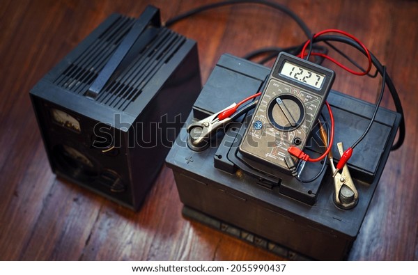 Check and\
charg car battery with charger from home electricity. Person\
measures voltage. Voltmeter to check voltage level on car battery.\
Car battery maintenance - 12v, low\
battery