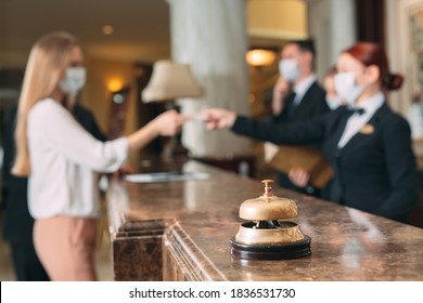 Check In Hotel. Receptionist At Counter In Hotel Wearing Medical Masks As Precaution Against Virus. Young Woman On A Business Trip Doing Check-in At The Hotel