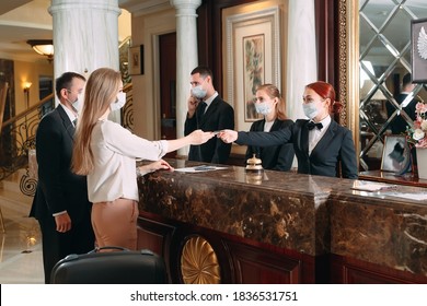 Check In Hotel. Receptionist At Counter In Hotel Wearing Medical Masks As Precaution Against Virus. Young Woman On A Business Trip Doing Check-in At The Hotel