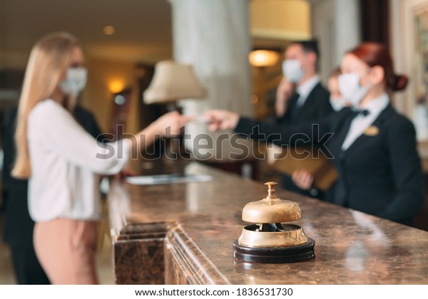 Check in hotel. receptionist at\
counter in hotel wearing medical masks as precaution against virus.\
Young woman on a business trip doing check-in at the\
hotel