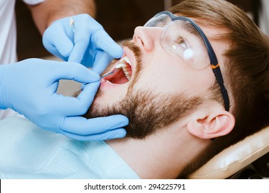 Check And Select The Color Of The Teeth In The Dentist Chair. Dentist Makes The Process Of Treatment Of Handsome Young Man.