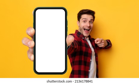 Check This Ad. Cheerful Emotional Man Holding And Pointing At Big Blank Smartphone With White Screen In Hand, Happy Millennial Guy Recommending New Application Or Mobile Website, Mockup Banner Collage