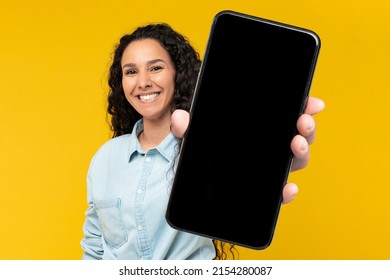 Check This Ad. Cheerful Woman Holding Big Blank Smartphone With Black Screen In Hand, Happy Millennial Lady Recommending New Application Or Mobile Website, Mockup Banner Collage, Yellow Orange Wall