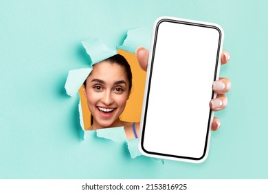 Check This App Advert Offer. Excited lady holding big smartphone with isolated white screen in hand, showing close to camera through torn paper hole, presenting device with empty free space for mockup