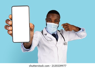 Check This App. Black Doctor Wearing Medical Mask Pointing At Big Blank Smartphone In His Hand, Excited African American Therapist Demonstrating Copy Space For Medical App, Collage, Mockup Image