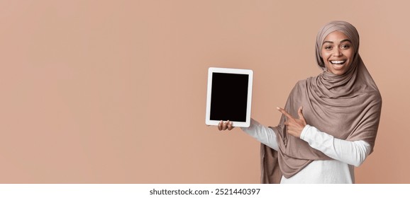 Check This App. Joyful Black Muslim Woman Pointing At Digital Tablet With Black Screen In Her Hands, Posing Over Yellow Background, Copy Space - Powered by Shutterstock