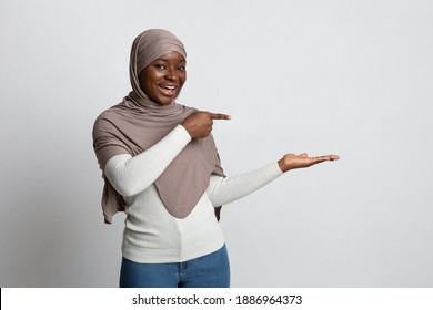 Check This. Excited Black Islamic Woman In Hijab Pointing At Something In Her Empty Palm, Cheerful Religious African Muslim Lady In Headscarf Demonstrating Free Copy Place For Your Design, Mockup