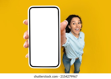 Check This Great App. Emotional Woman Holding Big White Empty Smartphone Screen In Hand Showing Cellphone Display Close Up To Camera, Recommending App On Orange Studio Wall. Above High Angle Top View