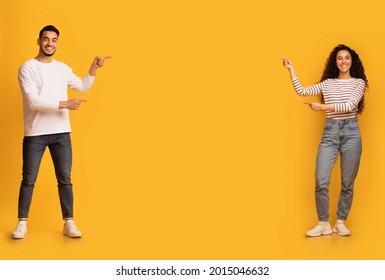 Check This. Happy arab couple pointing at copy space in the middle of yellow background, young middle eastern man and woman recommending something, showing free place for your design or advertisement