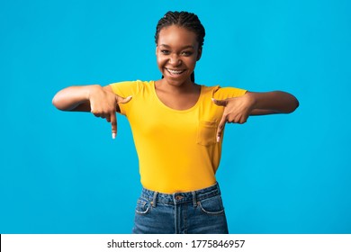 Check This Out. Cheerful African Girl Pointing Fingers Down Posing Standing Over Blue Background. Studio Shot