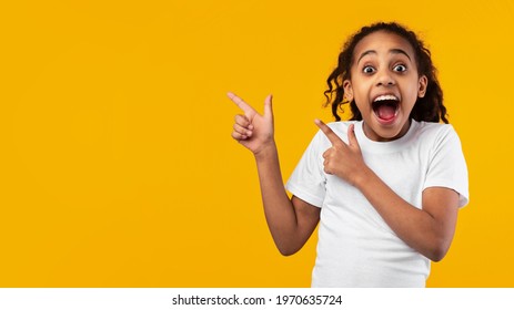 Check This. Portrait Of Excited Black Young Girl Pointing With Two Fingers Aside At Copy Space On Yellow Background, African American Kid Demonstrating Free Place For Your Design Or Advert, Banner