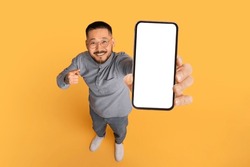 Check This. Smiling Asian Man Pointing At Big Blank Smartphone In His Hand, Happy Millennial Guy Advertising Online Offer Or Mobile App, Standing Over Yellow Studio Background, Collage, Mockup