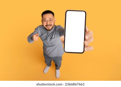 Check This. Smiling Asian Man Pointing At Big Blank Smartphone In His Hand, Happy Millennial Guy Advertising Online Offer Or Mobile App, Standing Over Yellow Studio Background, Collage, Mockup - Powered by Shutterstock