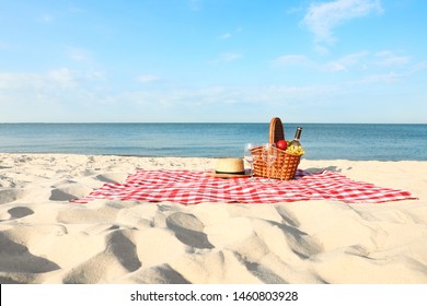 Checkered blanket with picnic basket and products on sunny beach
