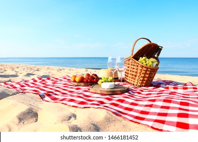 Checkered blanket with picnic basket and products on sunny beach. Space for text