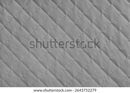 Checkered, diamond stitching pattern, gray quilted fabric background. Blanket or puffer jacket, stitch rhombus texture close up, macro. Wallpaper, backdrop.
