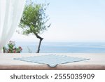 Checkered kitchen towel on wooden table with blurred blue sky seascape and white curtain as background