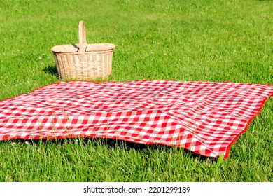 Checkered tablecloth and picnic basket on green grass - Powered by Shutterstock