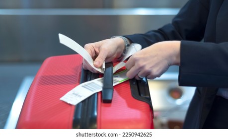 check-in employee attaches a luggage tag to suitcase of passenger - closeup of hands  - Shutterstock ID 2250942625