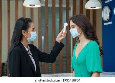 Check-in At The Hotel.Reception Wear Protective Face Mask Use Infrared Thermometer Checker Or Temperature Gun On Hotel Guest,Lifestyle New Normal After Corona Virus.