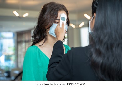 Check-in At The Hotel.Reception Wear Protective Face Mask Use Infrared Thermometer Checker Or Temperature Gun On Hotel Guest,Lifestyle New Normal After Corona Virus.