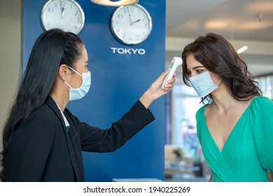 Check-in At The Hotel.Reception Wear Protective Face Mask Use Infrared Thermometer Checker Or Temperature Gun On Hotel Guest,Lifestyle New Normal After Corona Virus.