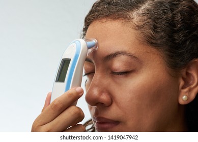 Checking body temperature theme. Young woman with digital thermometer next to forehead