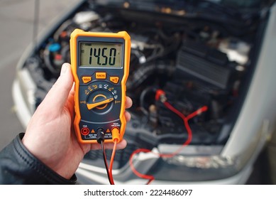 Checking car battery with digital multimeter. Check car battery using voltmeter. Man check up voltage level, alternator produce 14.5 volts with the engine idling. Winter service maintenance