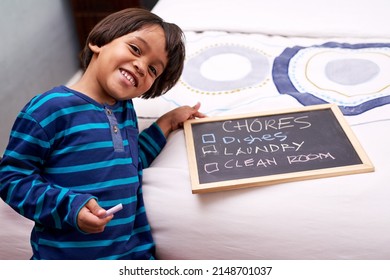 Checking the chores. Portrait of a young boy holding a chalkboard with chores written on.