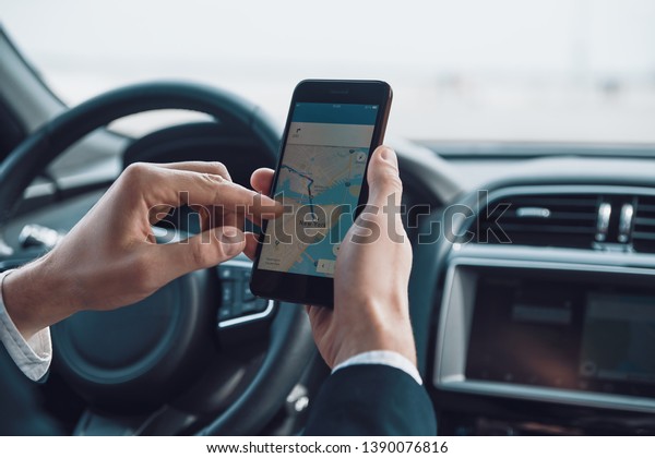 Checking the direction. Close up\
of young man using smart phone to check the map while driving a\
car