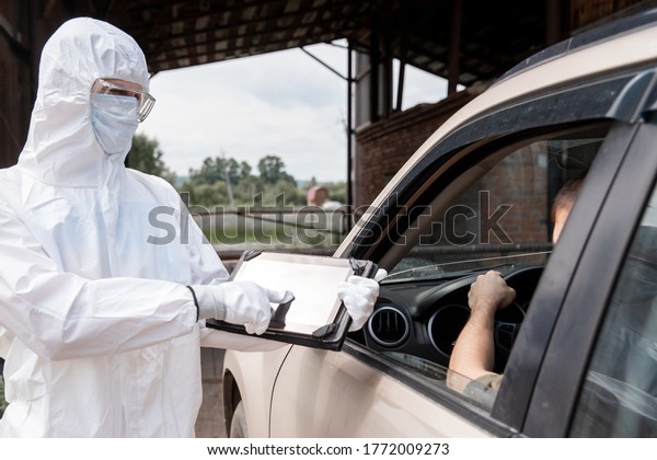 Checking and disinfecting car for virus COVID-19\
and bubonic plague border of city and country. Doctor in biohazard\
suit informs driver of\
danger.