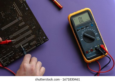 Checking The Electrical Resistance Of The Motherboard. Hands Using A Digital Multimeter To Test. View From Above. Selective Focus. Close-up